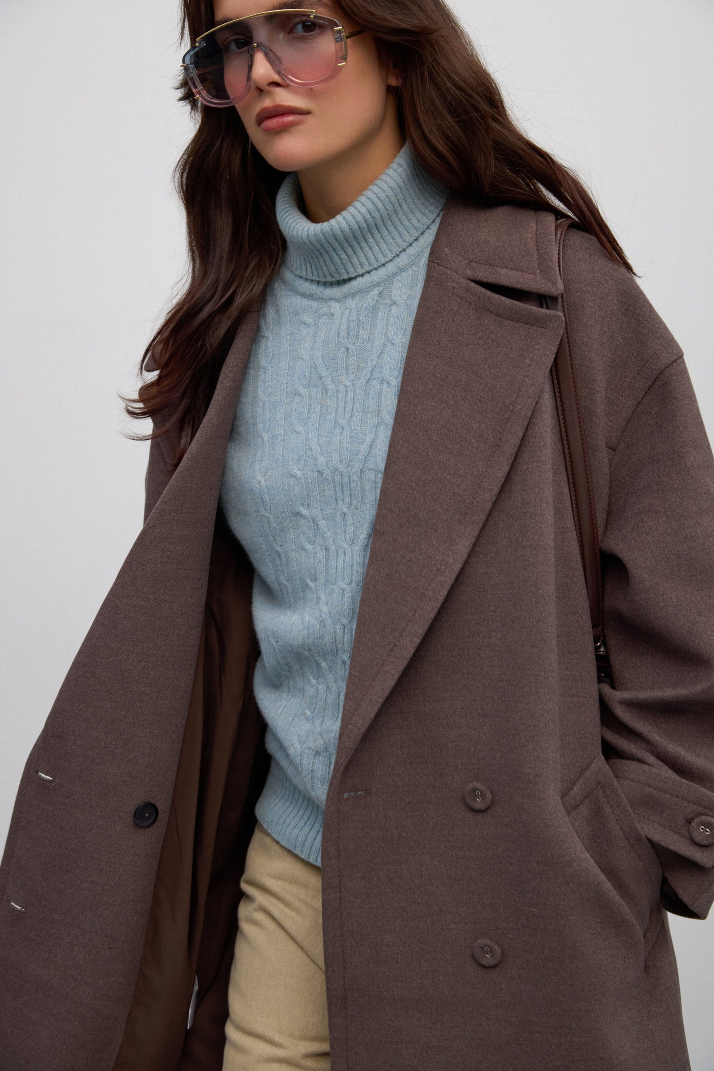 Brązowy, dwurzędowy płaszcz damski, wiązany w pasie, z szerokimi klapami.