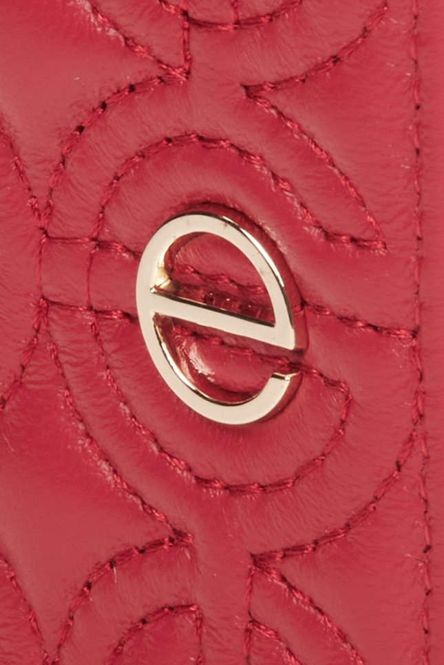 Mały, czerwony portfel damski ze skóry naturalnej - zbliżenie na tłoczone, złote logo.