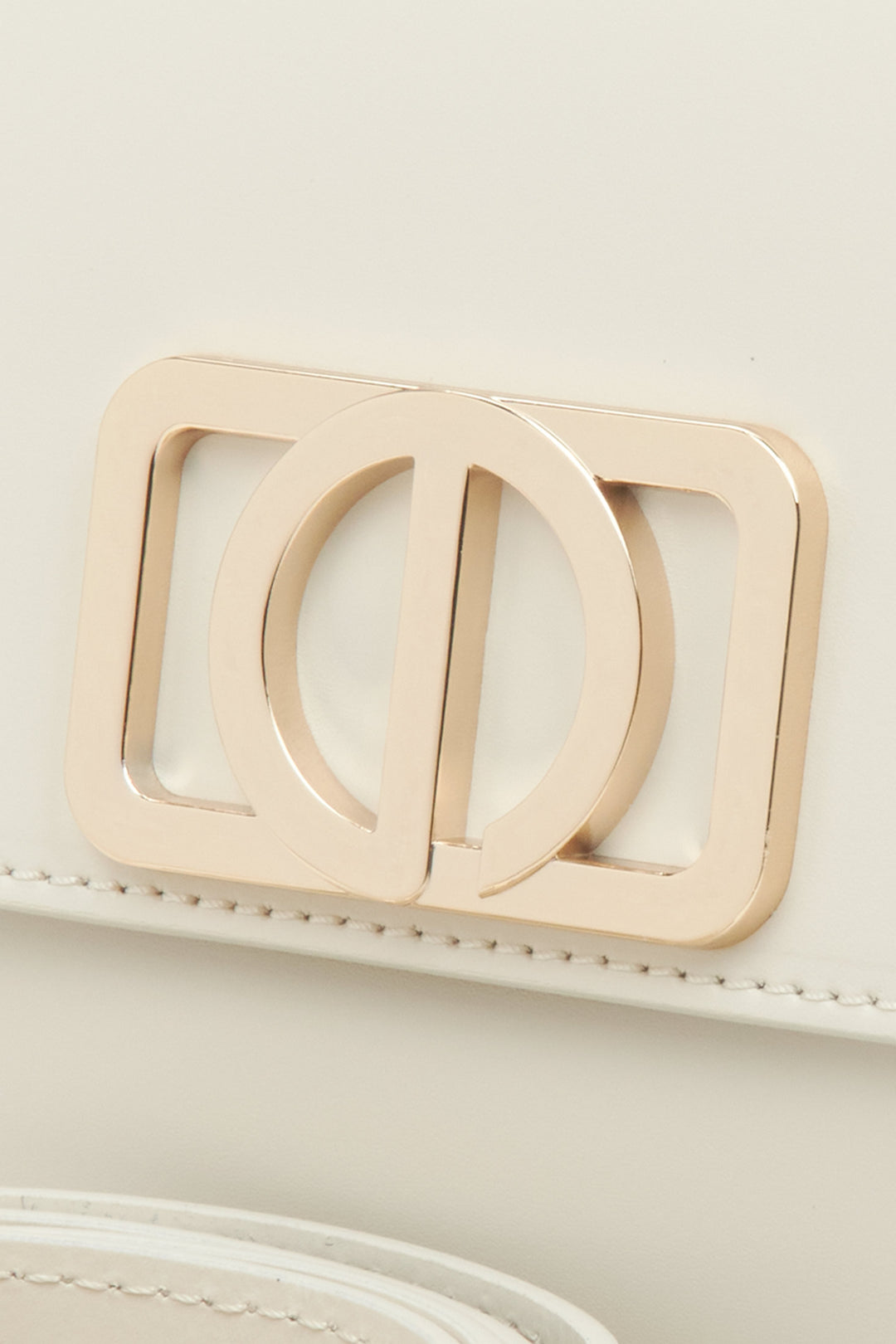 Kobieca torebka w odcieniu mlecznego beżu, o kompaktowym rozmiarze, w stylu bagietki - zbliżenie na detal.