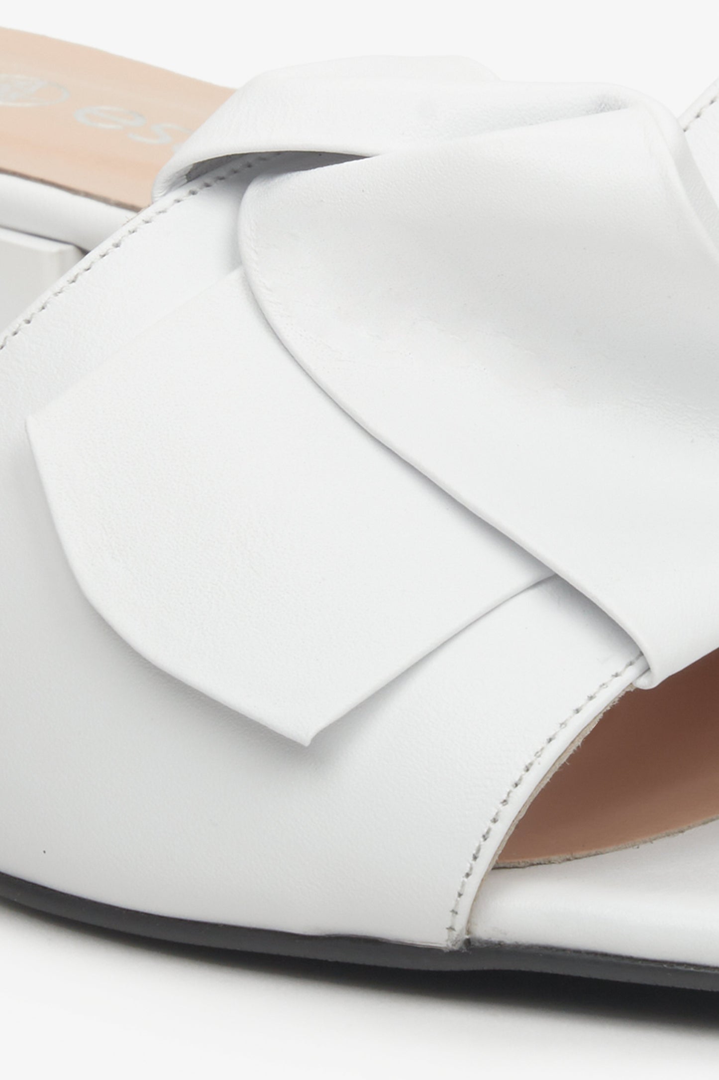 Skórzane, białe klapki damskie Estro z ozdobną kokardą - zbliżenie na ozdobę.