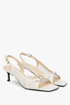 Białe sandałki typu slingback z ozdobną koronką na obcasie.