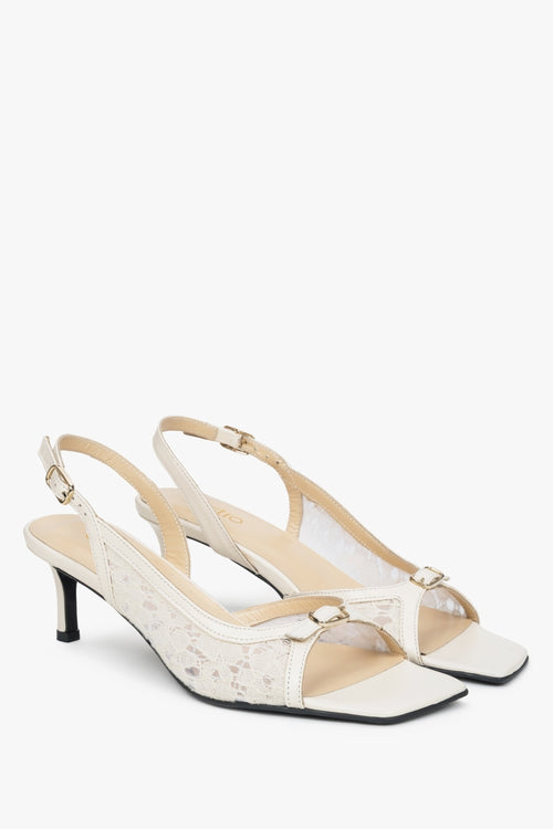 Białe sandałki typu slingback z ozdobną koronką na obcasie.