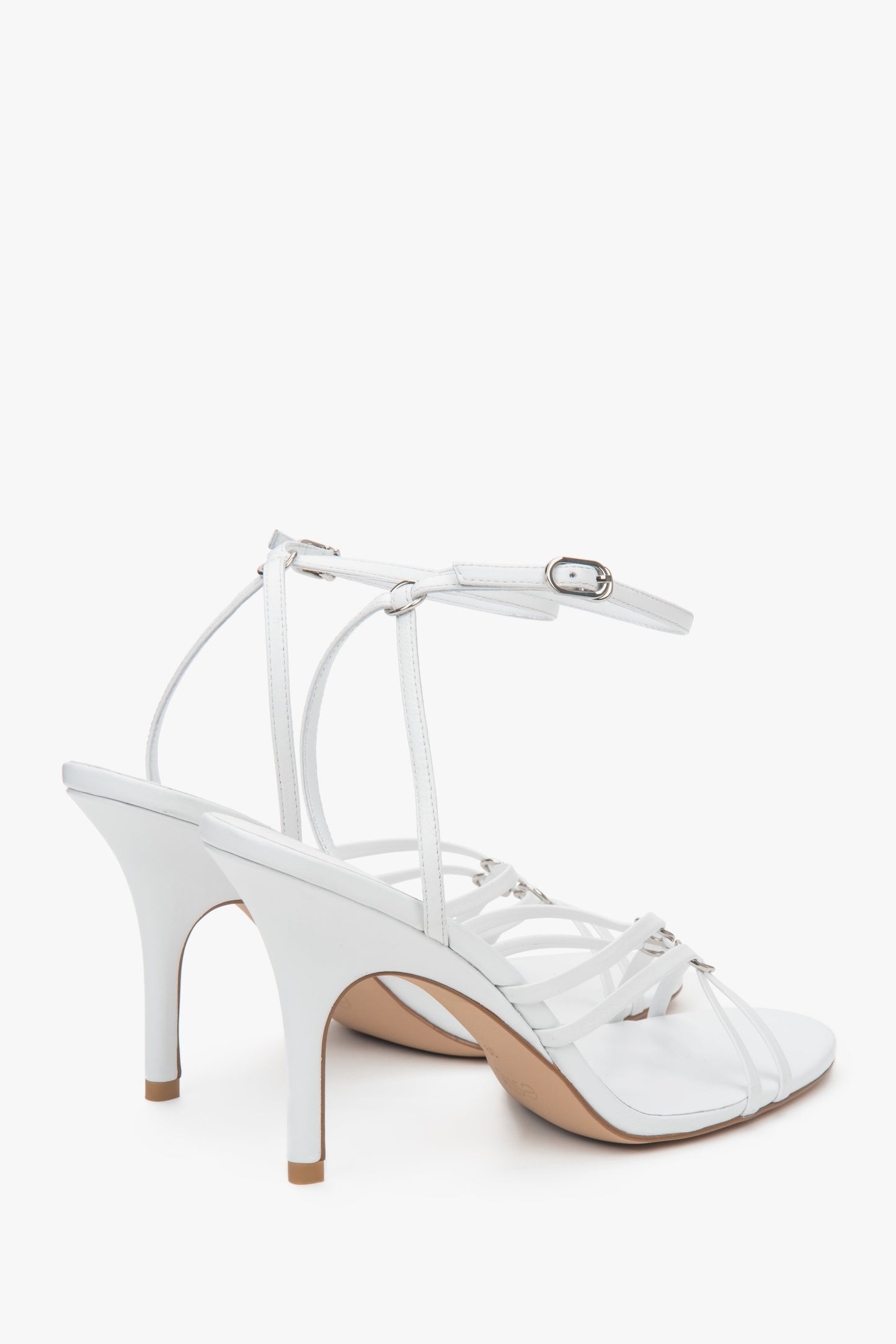 Na szpilce, białe skórzane sandały damskie ze srebrnymi detalami Estro.