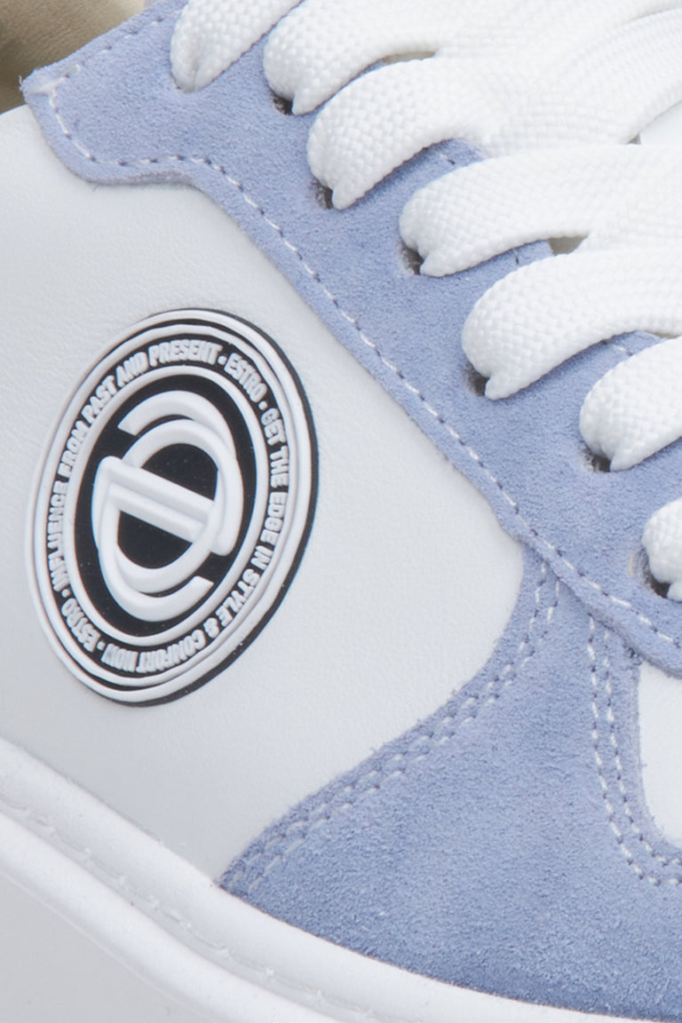 Sneakersy welurowo-skórzane Estro w kolorze biało-niebieskim. Zbliżenie na ozdobne logo.