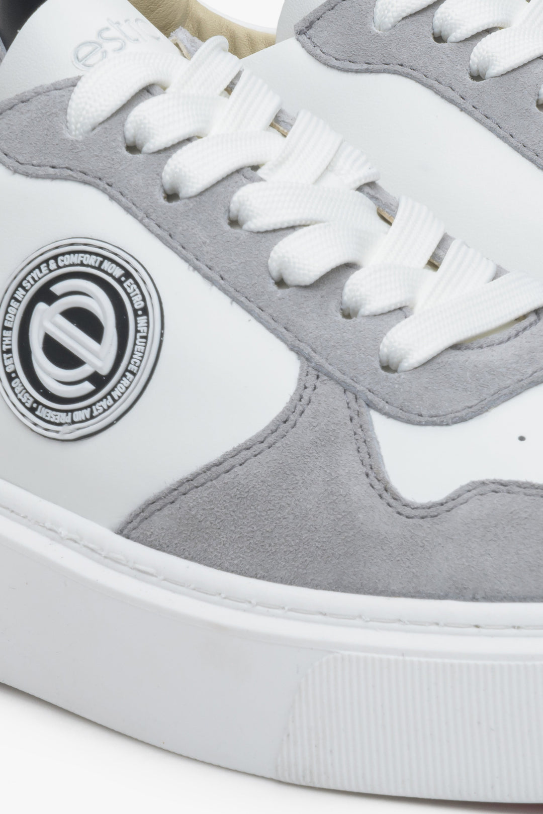 Sneakersy welurowo-skórzane Estro w kolorze biało-szarym. Zbliżenie na ozdobne logo.